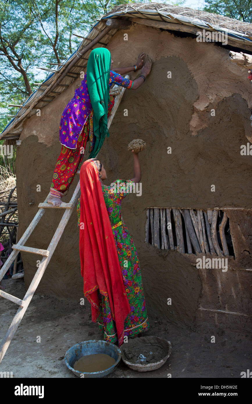Two women wearing traditional saris rendering a house wall with a mixture of clay, sand and cow dung, Rann of Kutch, Gujarat Stock Photo