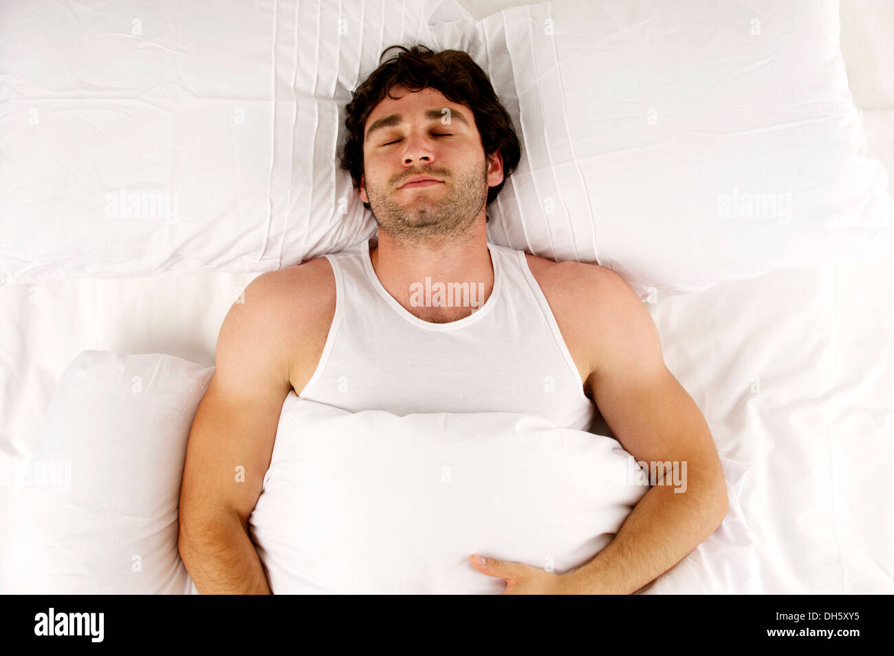 Handsome man laid sleeping enjoying a lie-in in the morning in a white bed Stock Photo