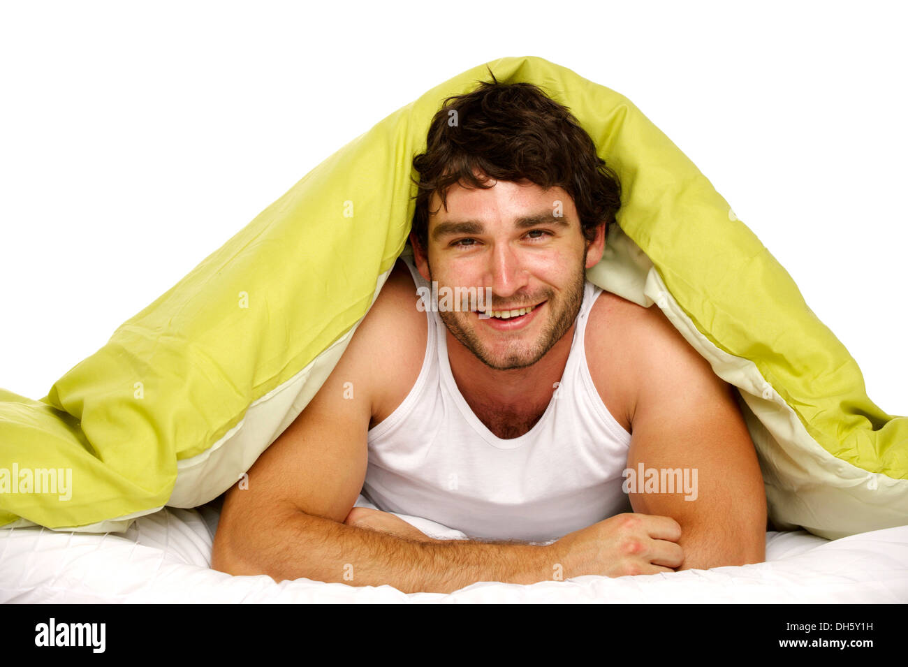 Attractive man laid in bed under a green duvet smiling at the camera Stock Photo