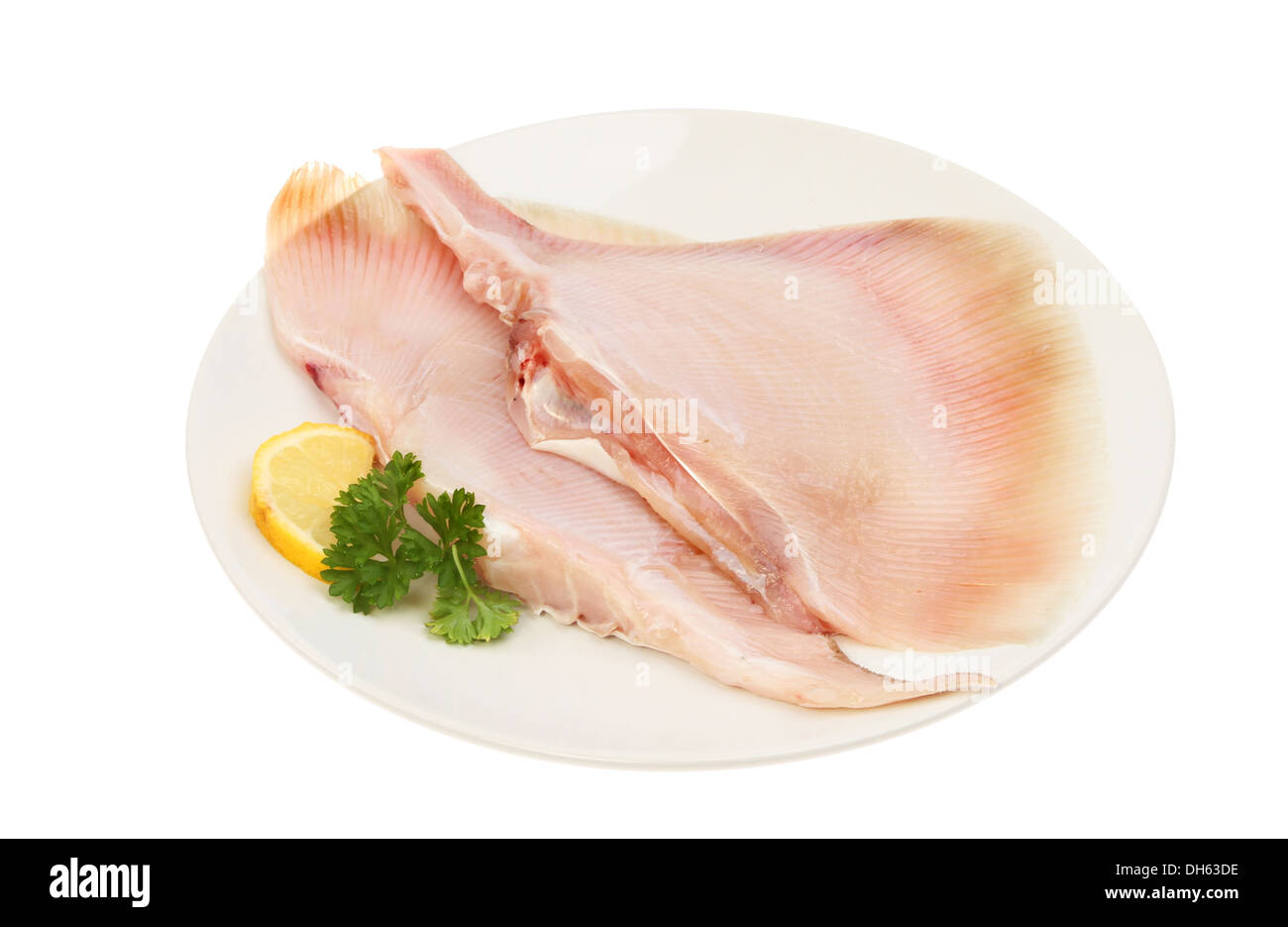 Two raw skate wings on a plate with lemon and parsley isolated against white Stock Photo