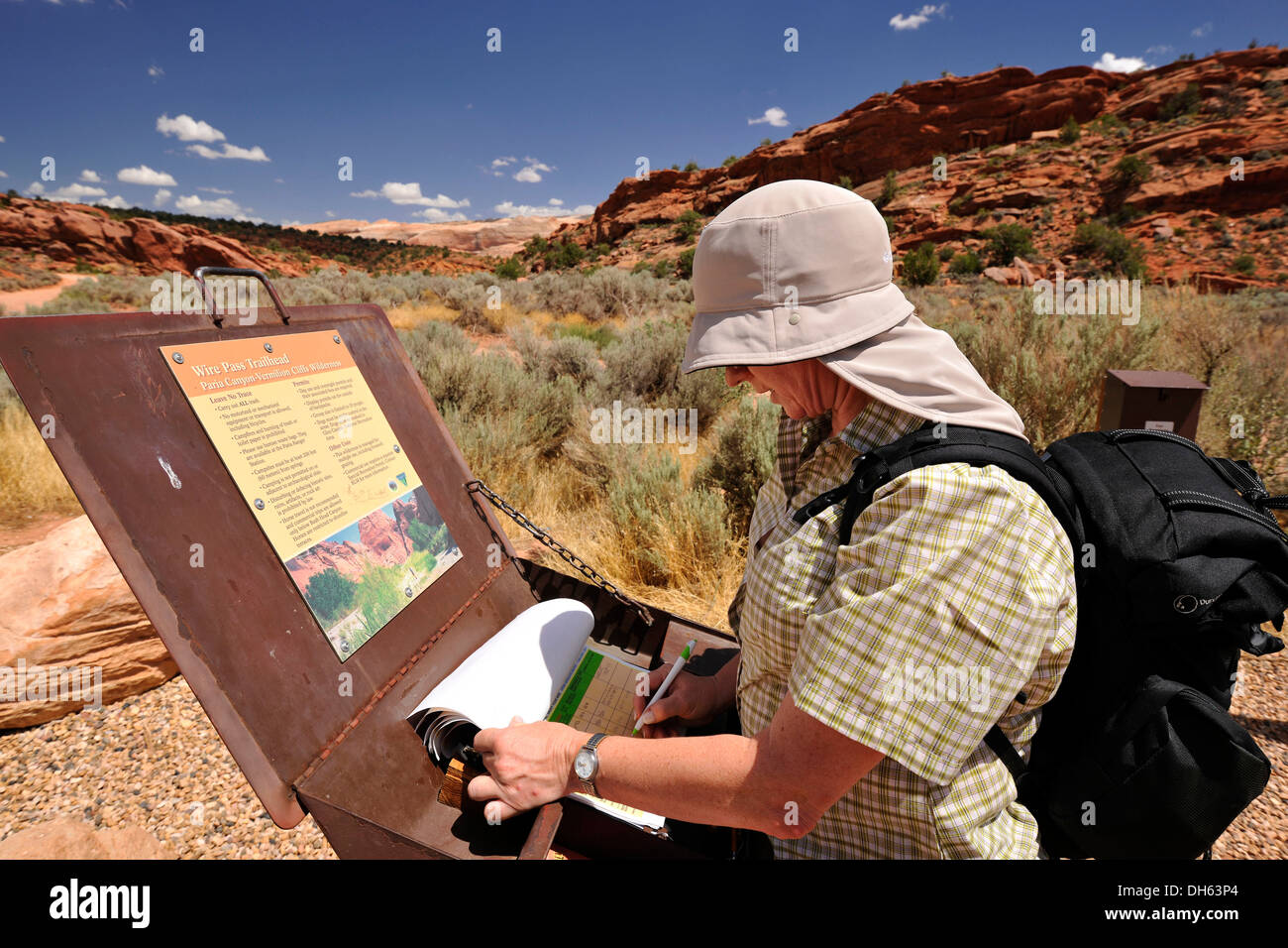 Tourist with a sun shield signing the registration box at Trailhead Wirepass, starting point to The Wave Navajo sandstone rocks, Stock Photo