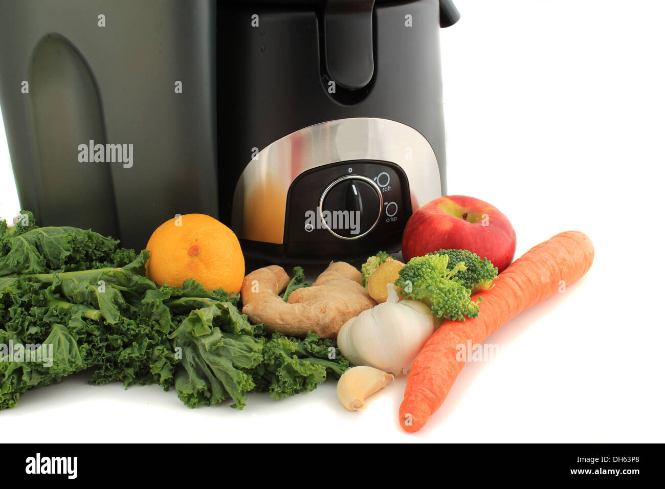 Juicer surrounded by healthy vegetables like carrots, ginger, and kale, ready to make juice Stock Photo