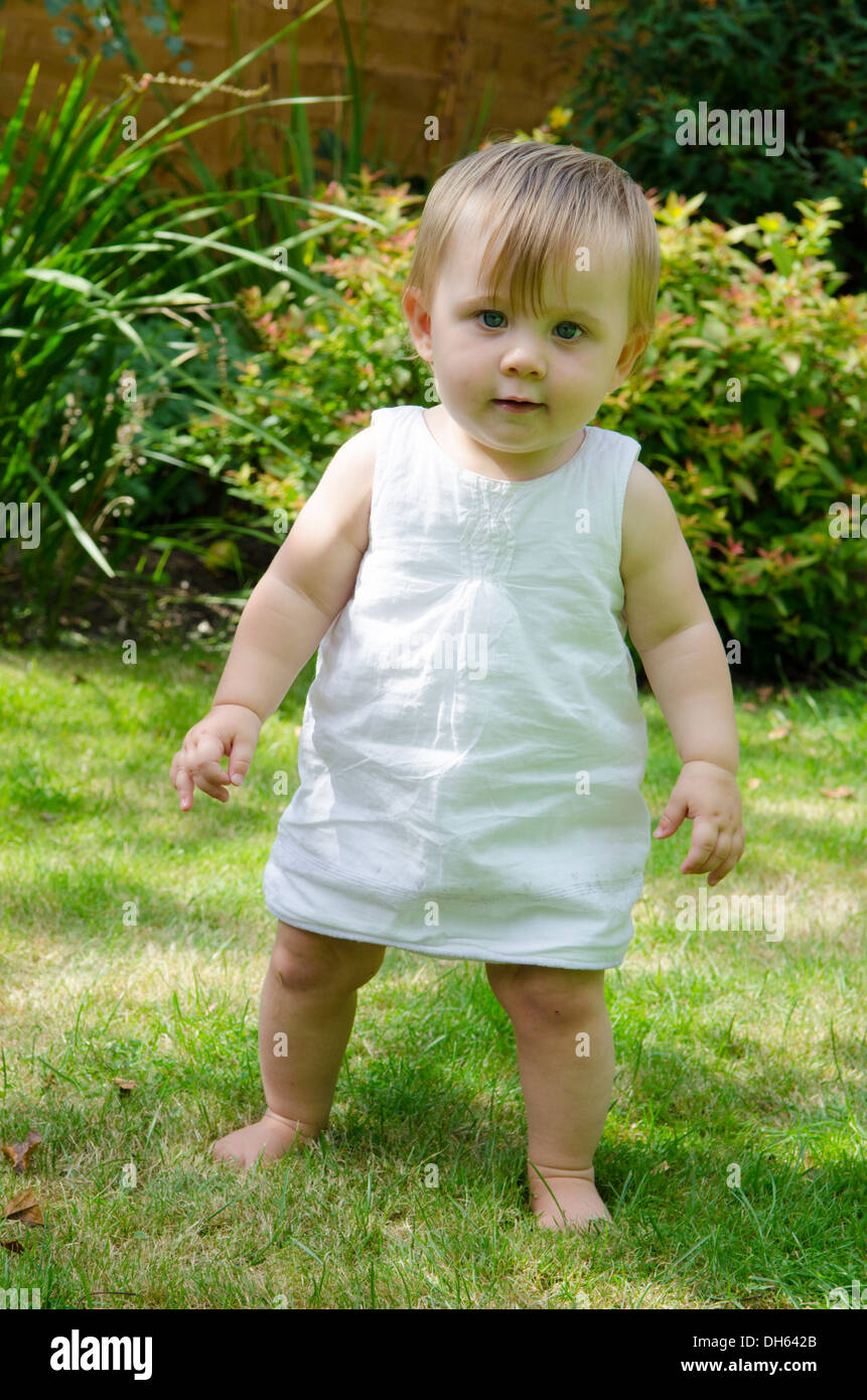 Nine month old girl learning to stand and walk on grass in garden.  England, UK. Stock Photo