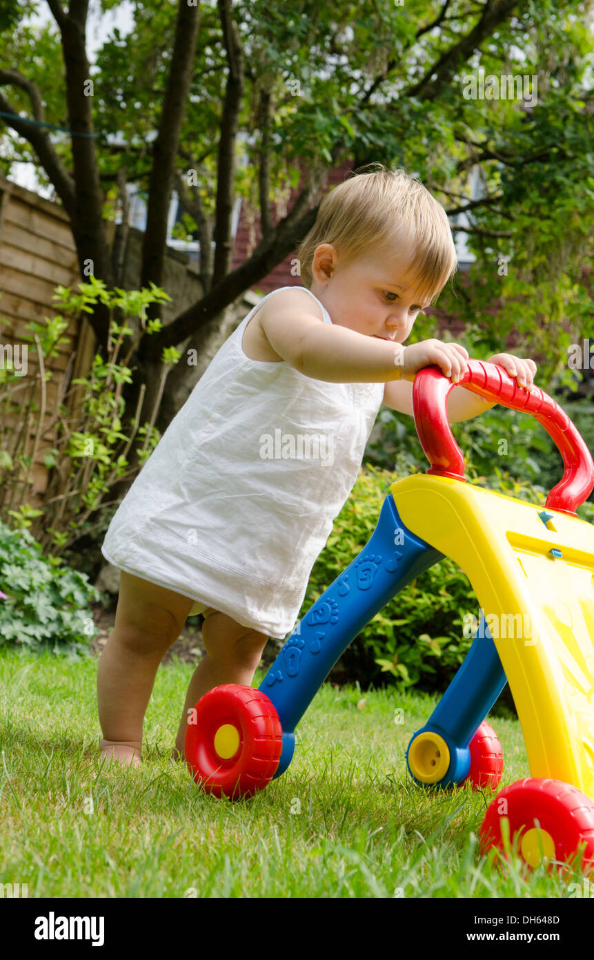 nine month old girl learning to walk with baby walker toy in garden. England, UK. Stock Photo