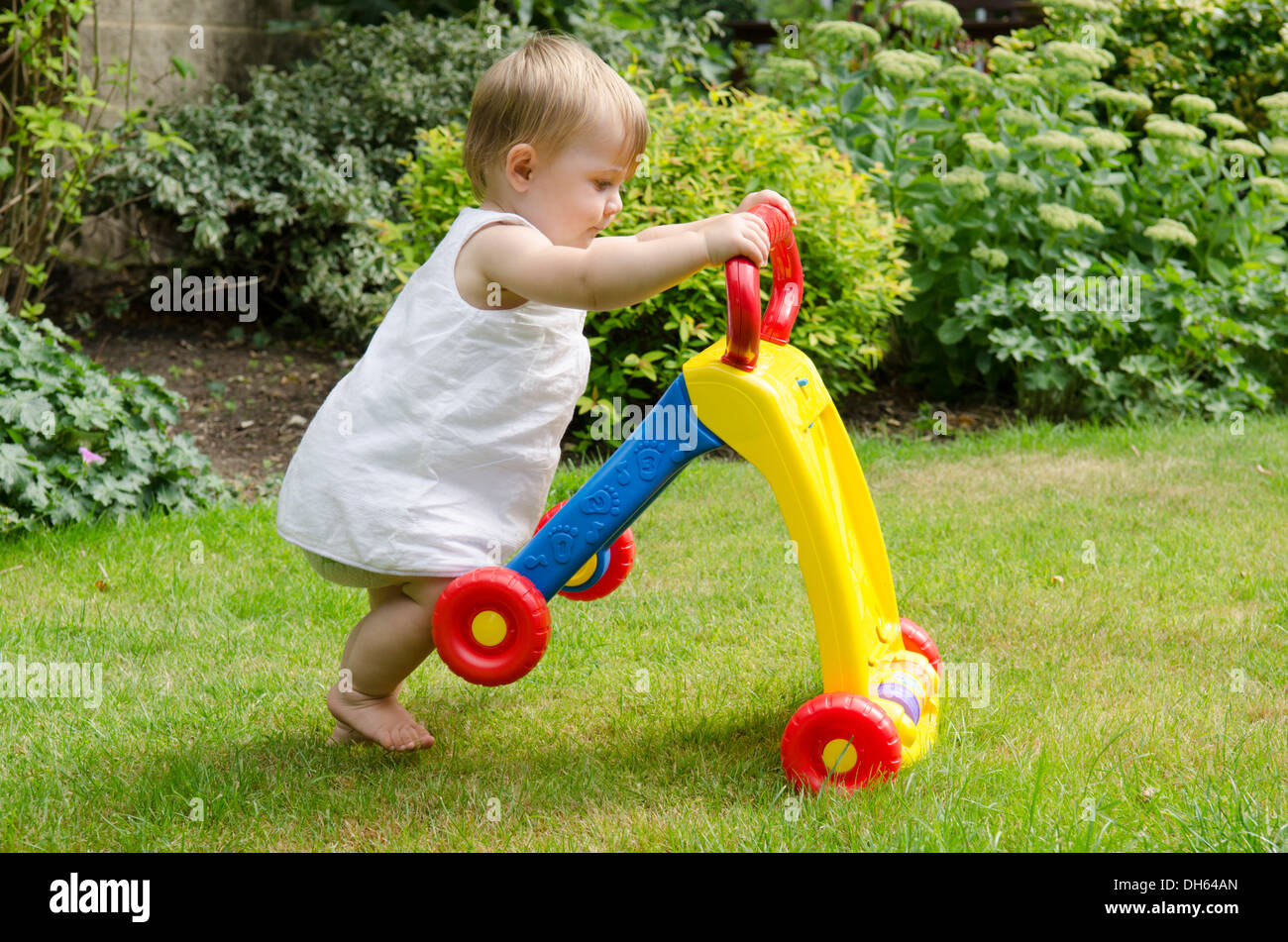 nine month old girl learning to walk with baby walker toy in garden. England, UK. Stock Photo