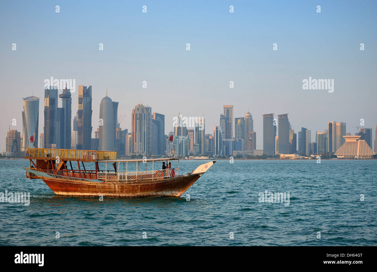 Tradition and modernity in comparison, dhow, a wooden cargo ship, in the evening light in front of the skyline of Doha Stock Photo