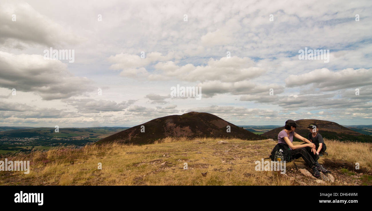 mother and son resting on the summit of Western Eildon with the other two summits in the background, Melrose Stock Photo