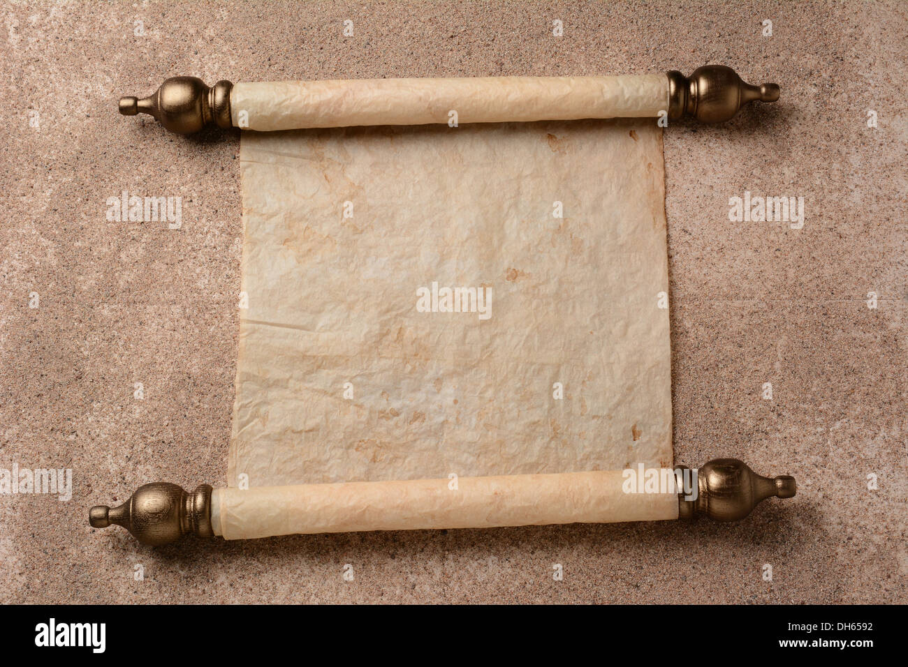 A rolled out scroll of parchment on a sand covered floor. The paper is blank ready for your copy. Stock Photo