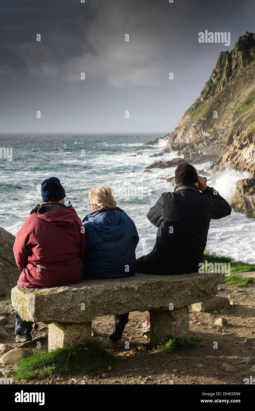 Three people sitting on a bench overlooking Porth Nanven in Cornwall. Stock Photo