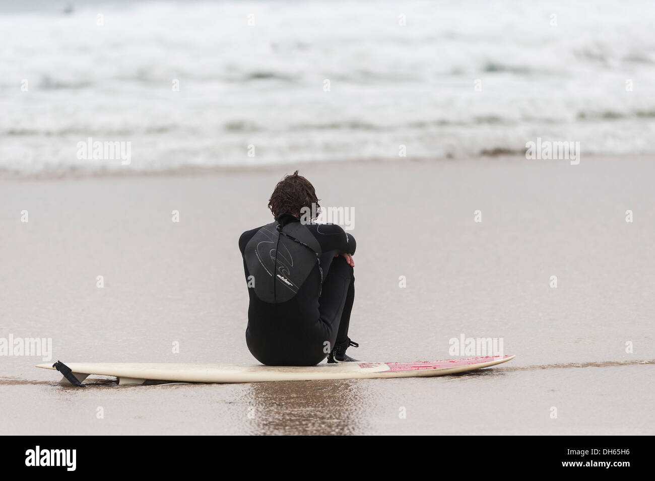 A surfer sitting on Fistral Beach in Newquay. Stock Photo