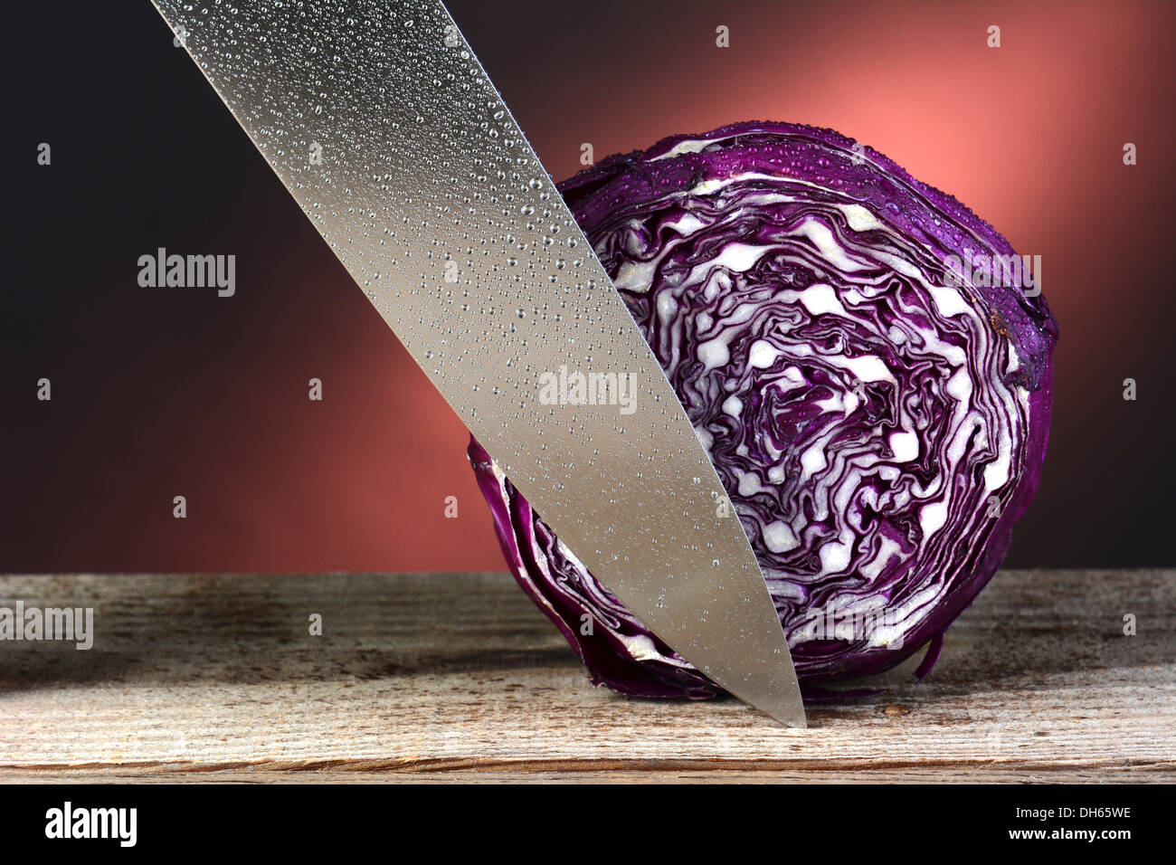 Closeup of a head of red cabbage and a carving knife. Horizontal format on a rustic wood surface and a warm background. Stock Photo