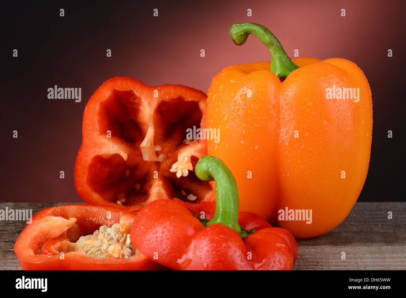 Closeup of an orange and red bell pepper on a rustic wood surface with a warm light to dark background. Stock Photo