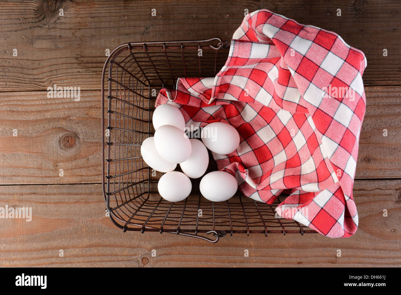 A wire basket with eggs and a red checkered napkin on a rustic wood surface. Stock Photo