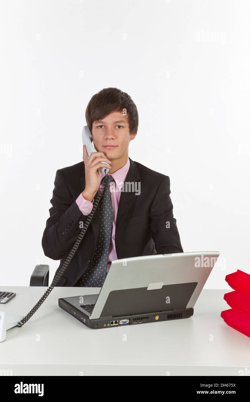 Young man sitting at a laptop and holding a phone Stock Photo