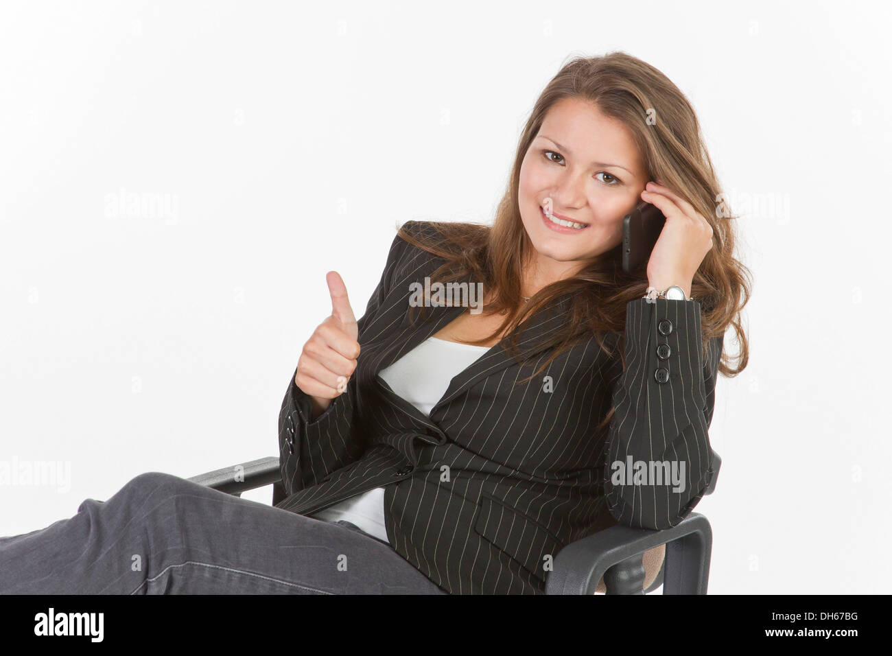 Young woman sitting on an office chair, making thumbs up gesture Stock Photo