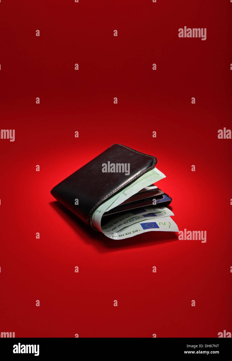 A black leather wallet filled with EU currency on a bright red background Stock Photo