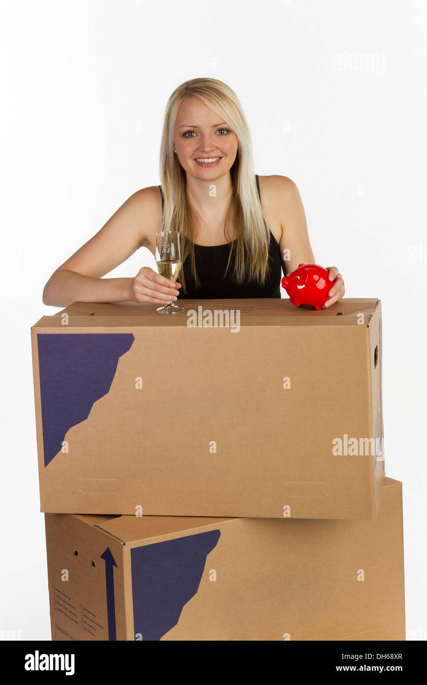 Young woman with moving boxes, glass of champagne and piggy bank Stock Photo