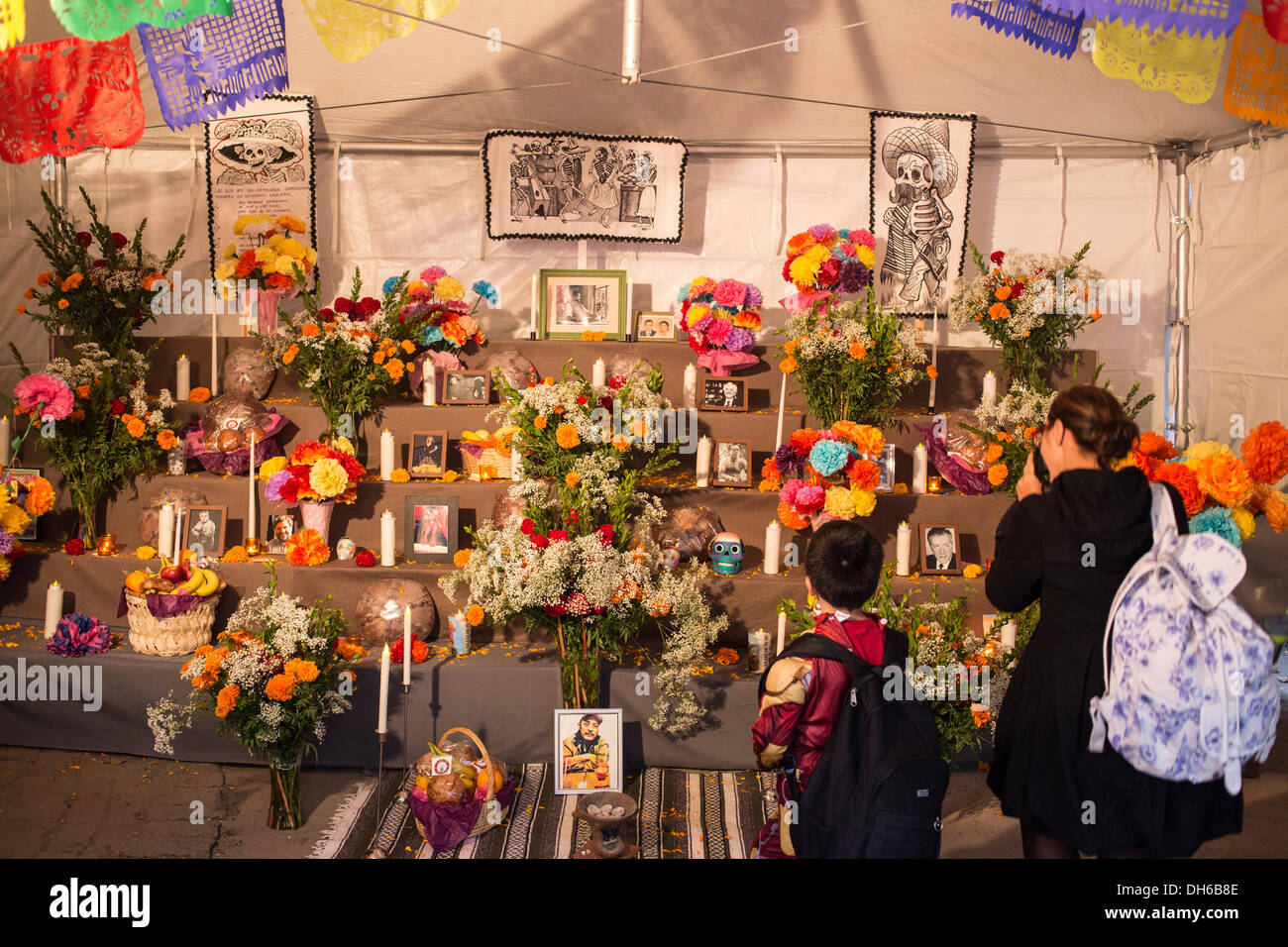 New York, NY, 31 October 2013. A woman and a boy stand in front of the public altar in a tent outside St. Mark's Church-in-the-Bowery on New York City's lower East Side. The black and white illustrations on the back wall are replicas of illustrations by José Guadalupe Posada, creator of the catrina, the woman's skull seen in the illustration on the left. Credit:  Ed Lefkowicz/Alamy Live News Stock Photo