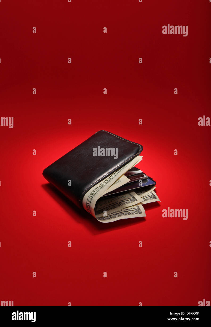 A black leather wallet filled with US currency on a bright red background Stock Photo