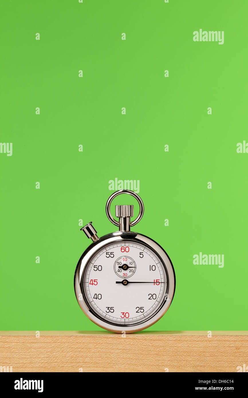 A stopwatch on a wooden shelf with a bright green background Stock Photo