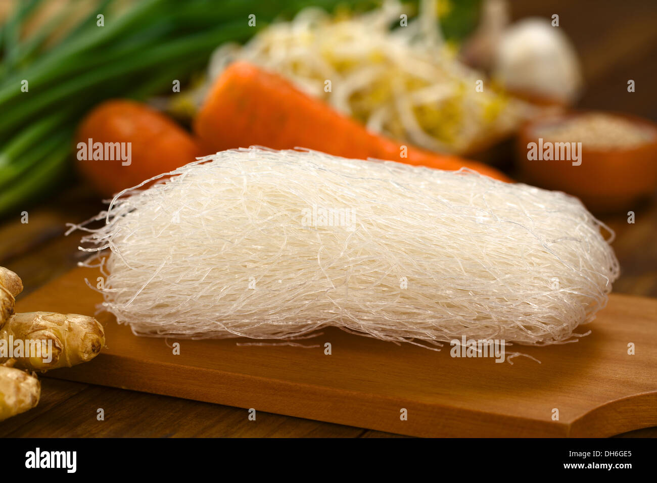 Raw rice noodles on wooden board with ginger and other vegetables (Selective Focus, Focus on the front of the noodles) Stock Photo