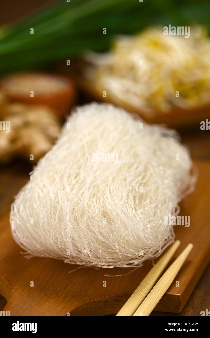 Raw rice noodles on wooden board with chopsticks on the side and vegetables in the back Stock Photo