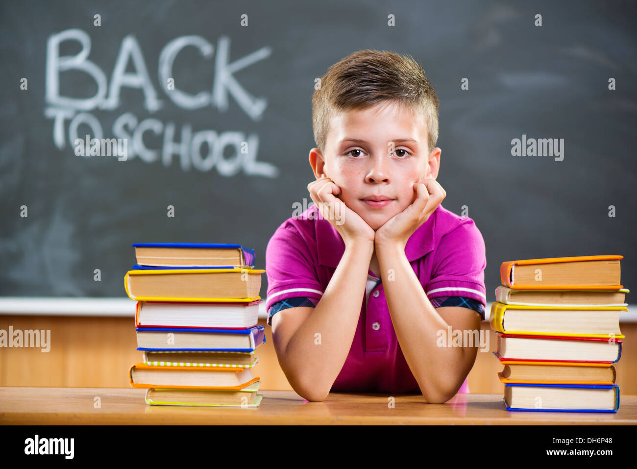 Cute pupil with pile of books in classroom Stock Photo - Alamy