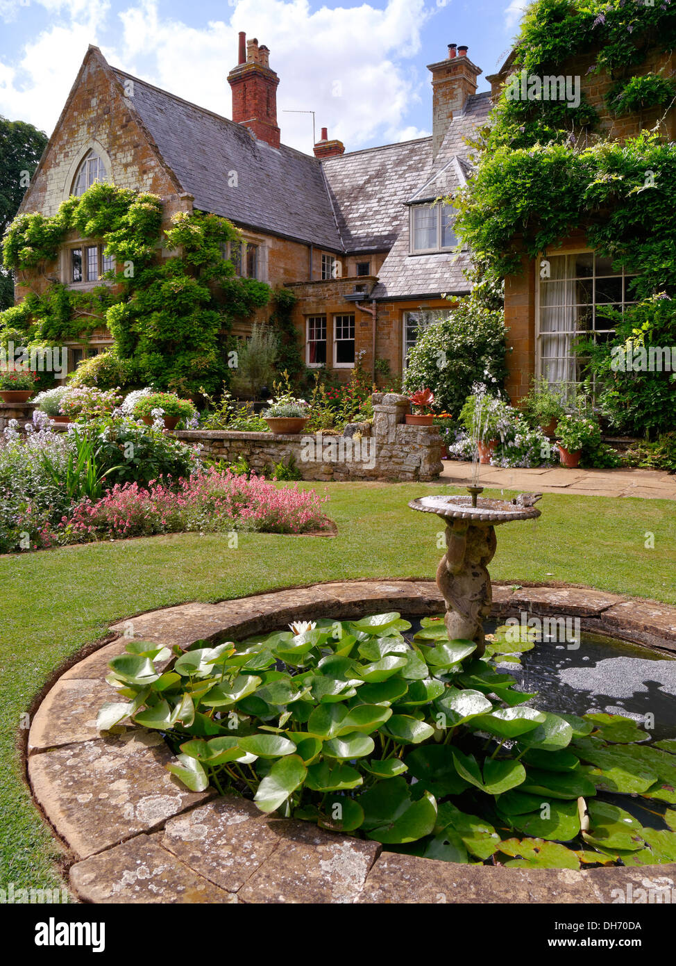 Small round ornamental garden pond and fountain set in gardens of Coton Manor House, Coton, Northamptonshire, UK. Stock Photo