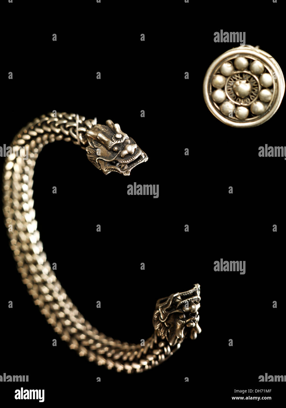Carved silver bracelet with dragon heads at both ends, together with a silver button Stock Photo