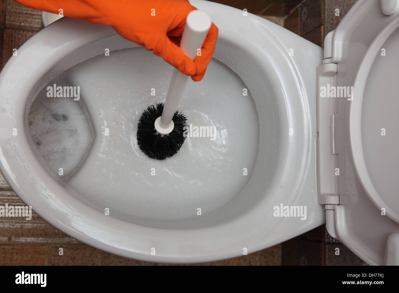 Female hand in orange rubber glove cleaning toilet bowl using brush