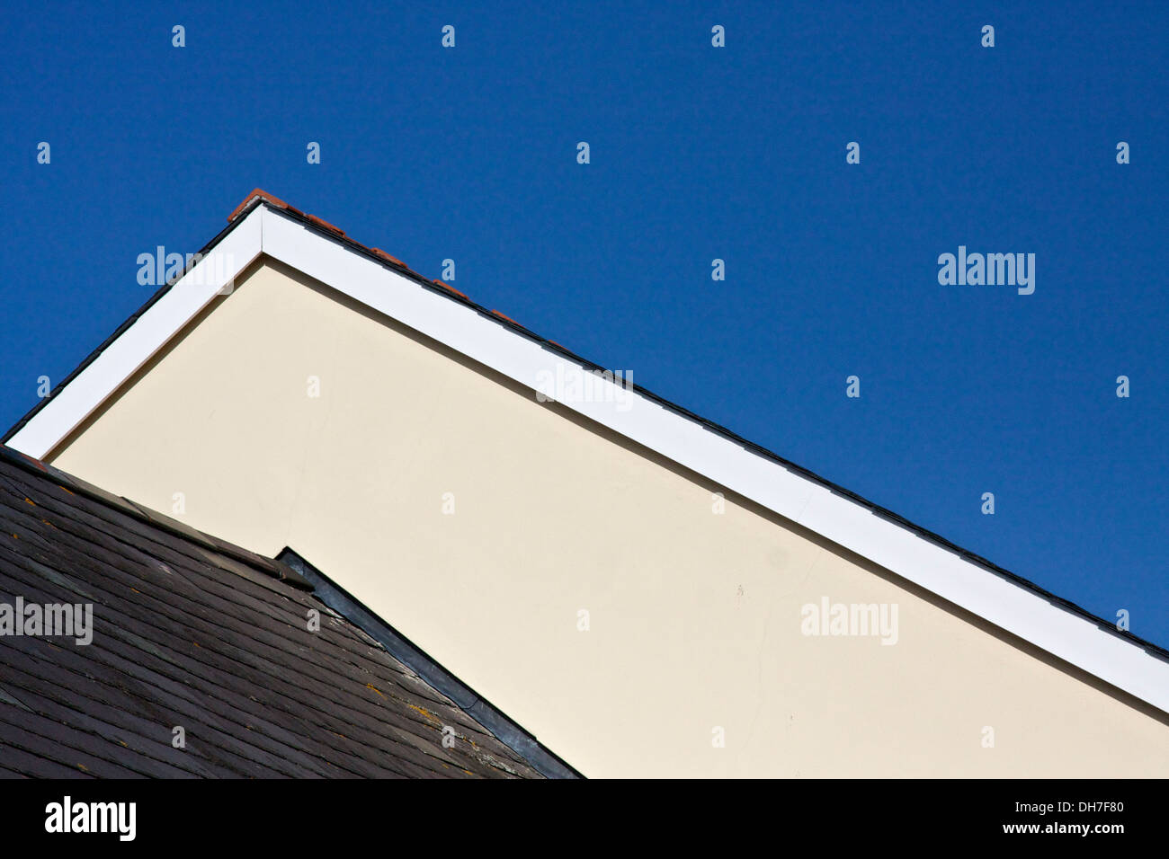 Gable end of a wall and pitched roof against deep blue sky. Stock Photo