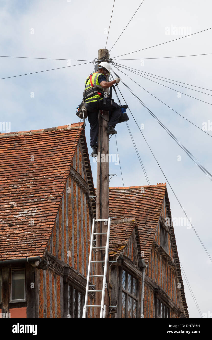 Telephone engineer working on wires at the top of a telegraph pole outside a in Lavenham, Suffolk, England, UK, Britain Stock Photo