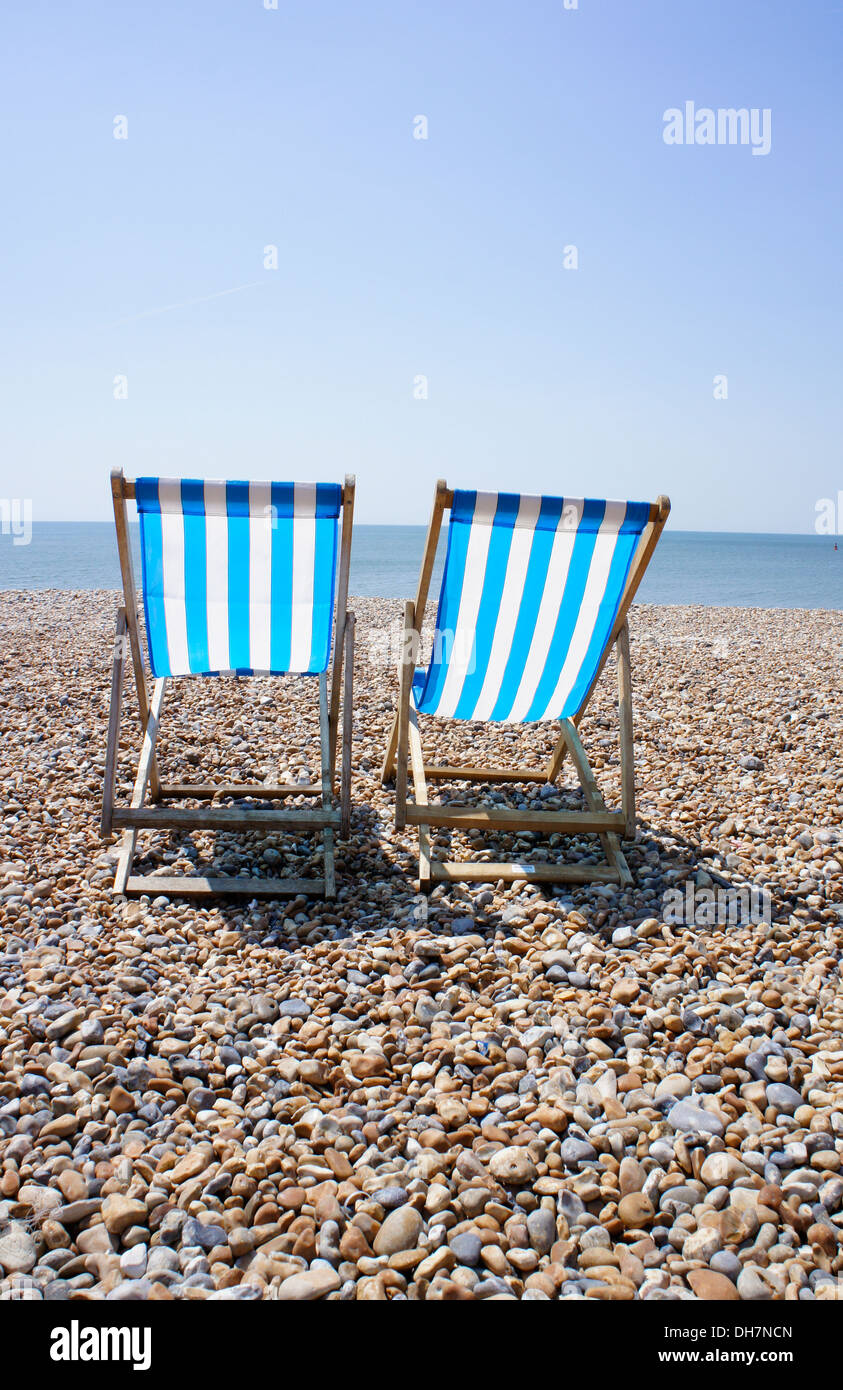 Stripy deck chairs on pebbly beach. Stock Photo