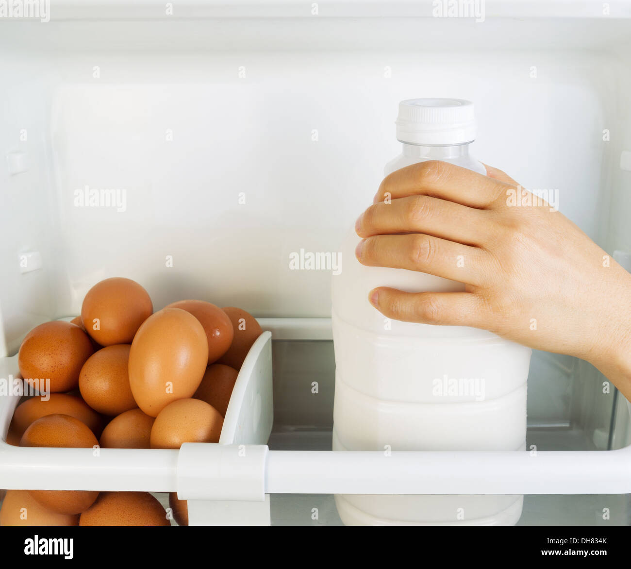 Photo of female hand grabbing milk container off of refrigerator door shelf with organic eggs off to the side Stock Photo