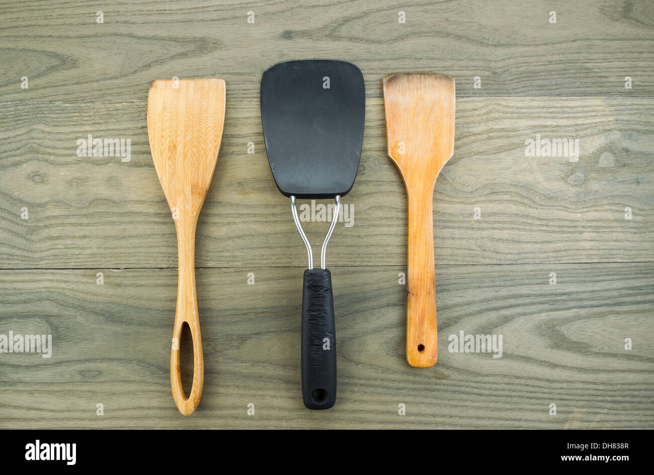 Horizontal photo of three kitchen spatulas, two of them wooden, on aged white oak boards Stock Photo