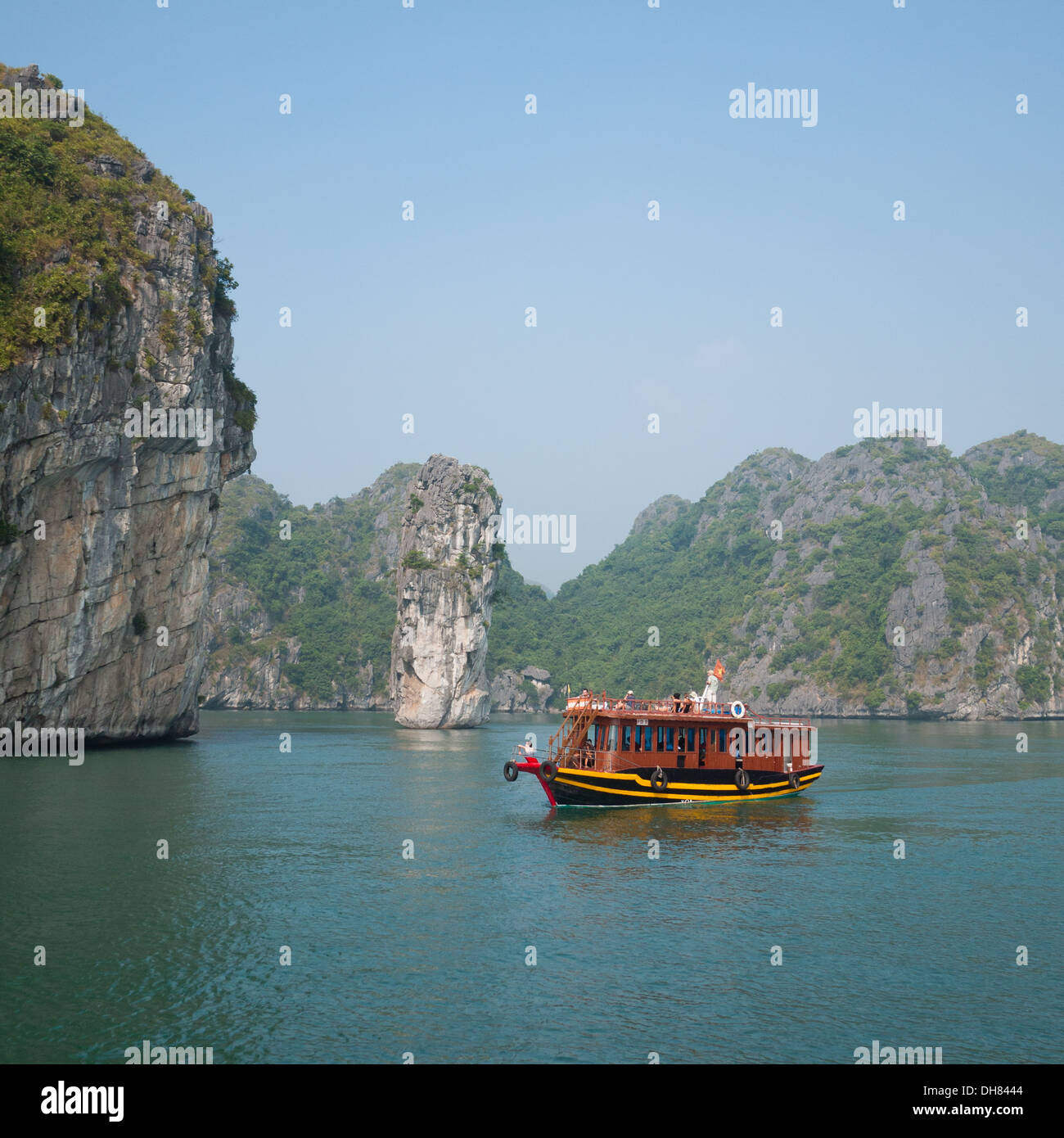 A view of a tourist boat moving by the spectacular limestone karst formations in Lan Ha Bay, Halong Bay, Vietnam. Stock Photo