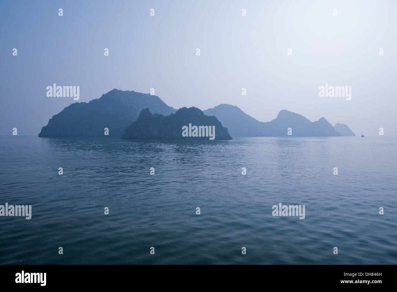 Mystical limestone formations in the distance just offshore Cat Ba Island in Lan Ha Bay, Halong Bay, Vietnam. Stock Photo