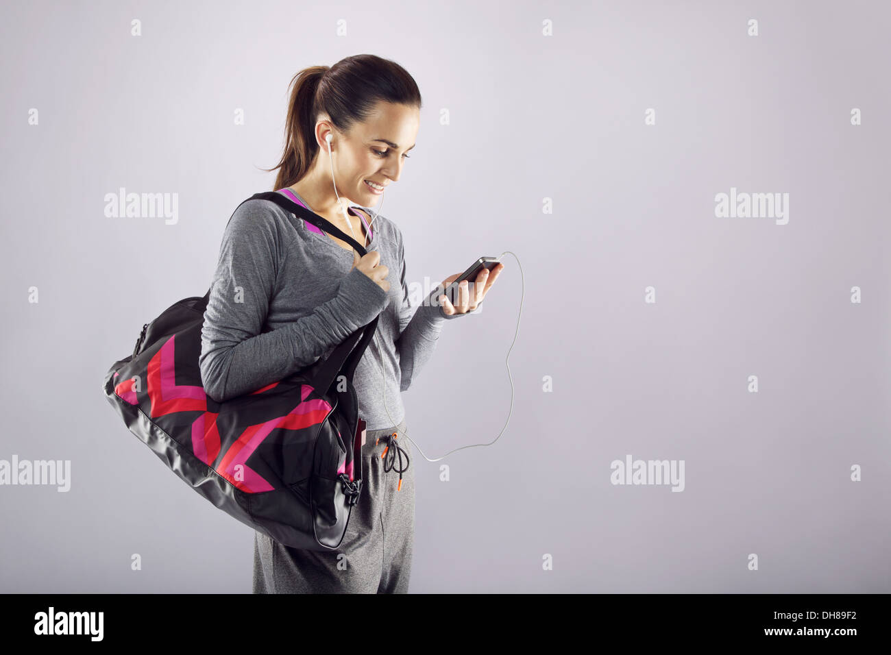 Good looking female athlete with a sports bag listening to music on her mobile phone. Fitness woman in sports clothing Stock Photo