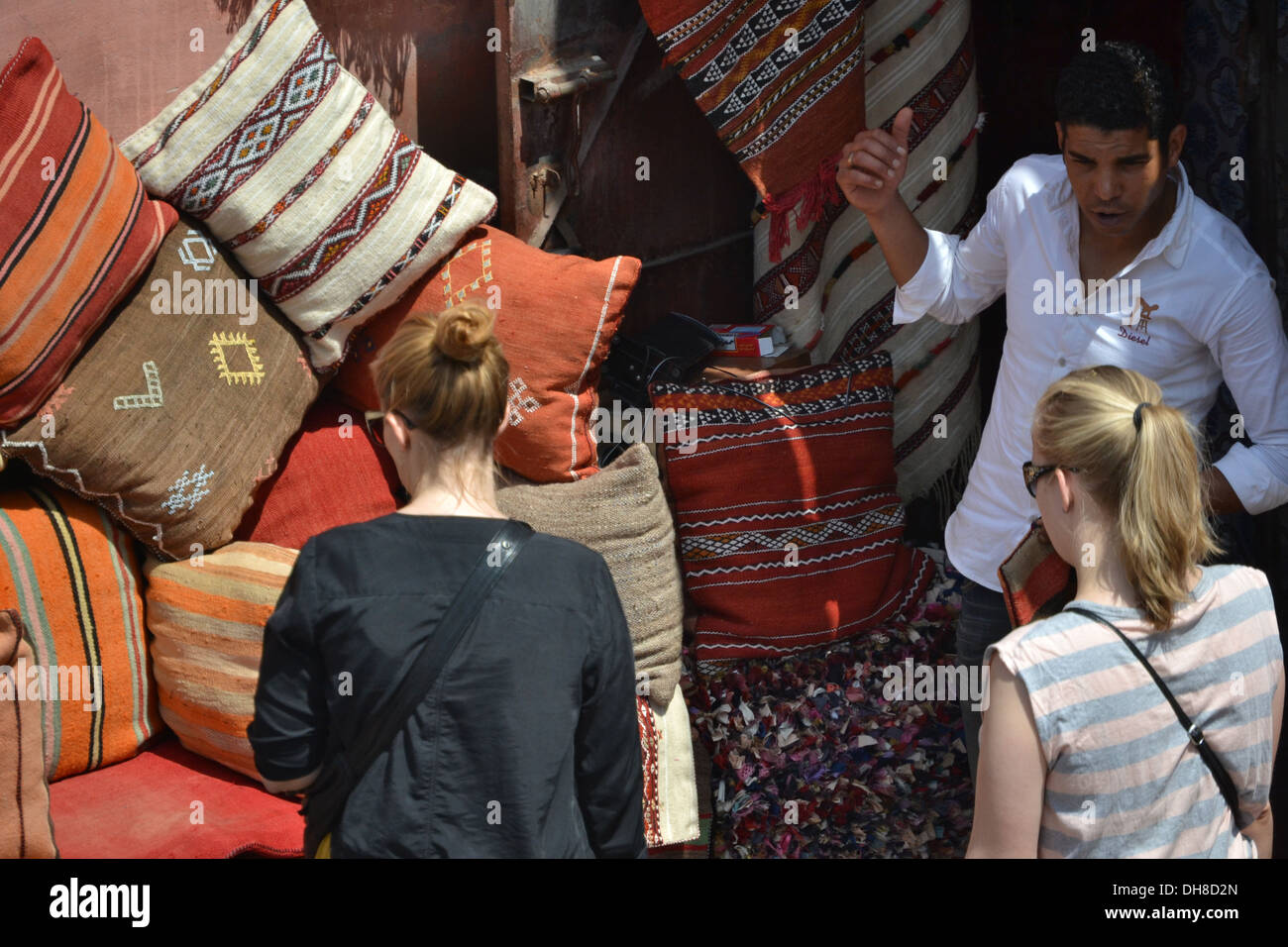 Marrakech market trader selling cushions to women tourists. Stock Photo