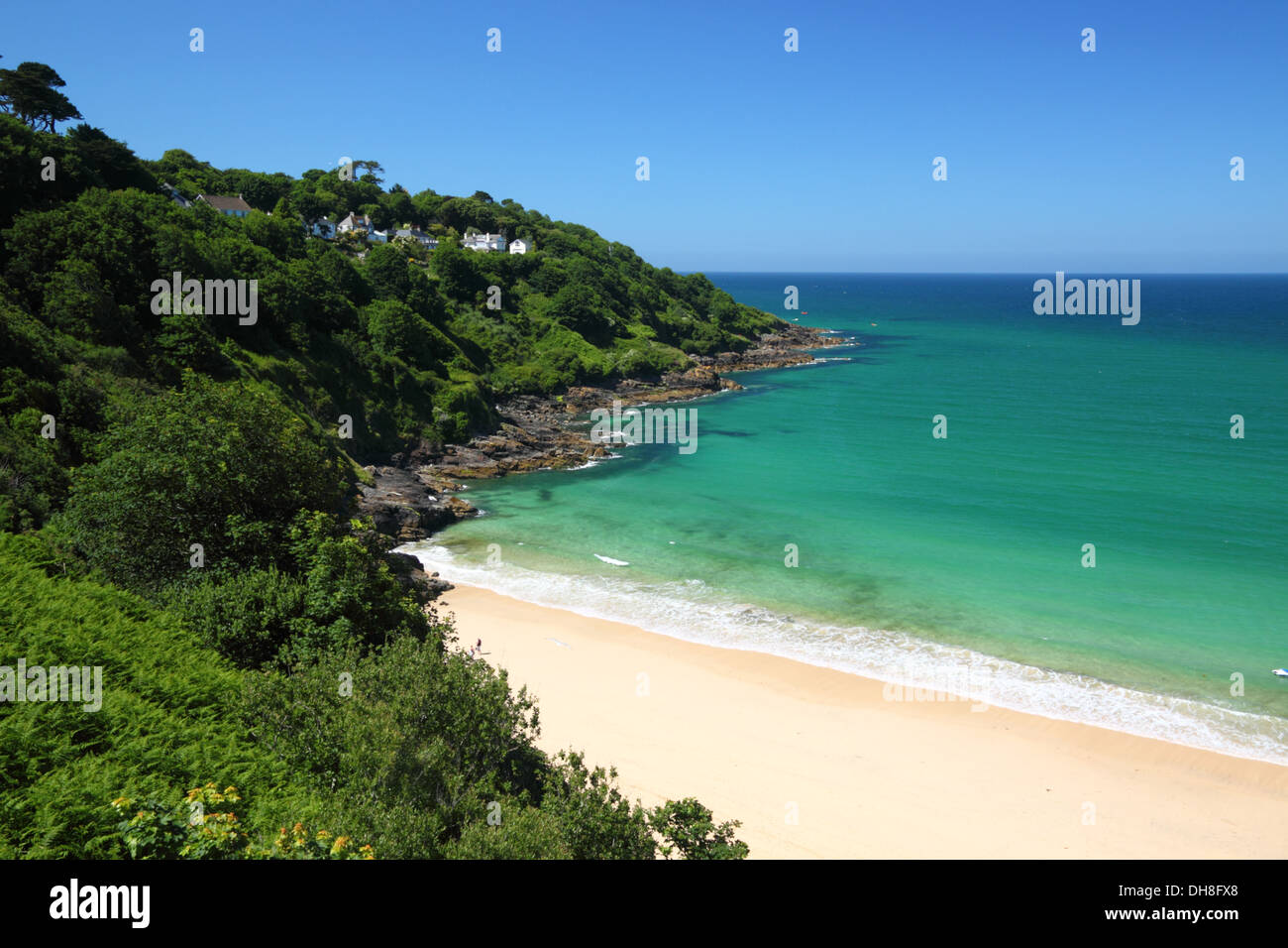 A golden sandy beach with turquoise blue sea and lush green cliffs. Stock Photo