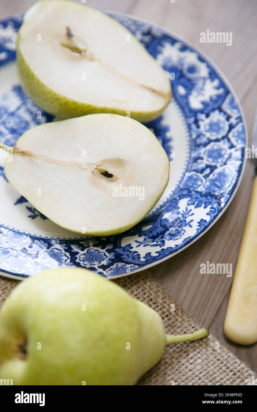 Two halves of cut green pear on a vintage blue and white patterned china plate resting on a wooden surface Stock Photo