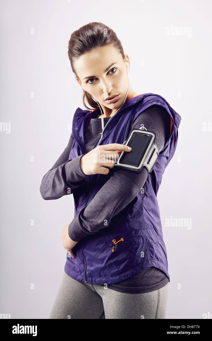 Fitness woman wearing earphones and mp3 player. Female runner listening music on grey background Stock Photo