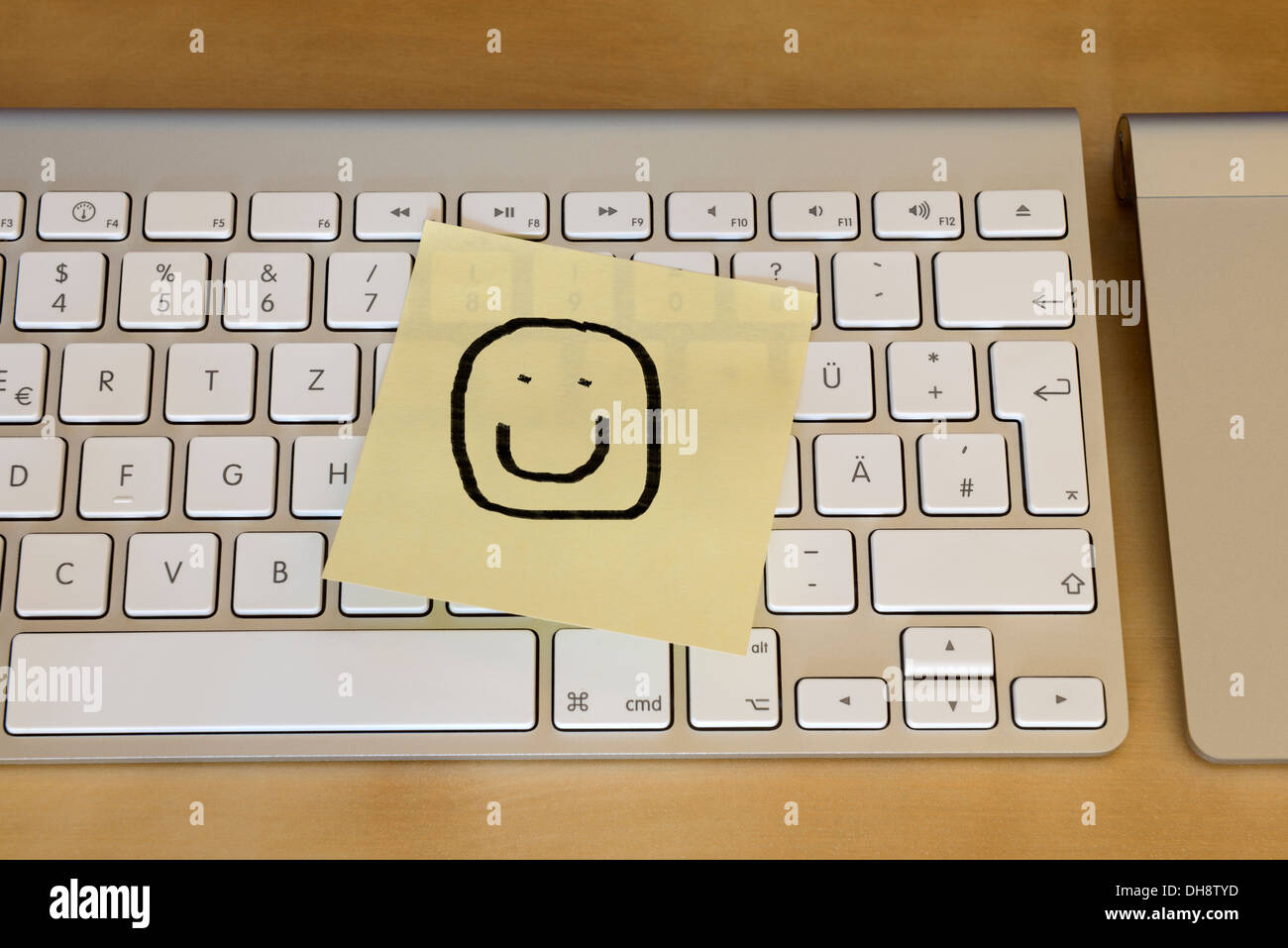 Post-it note smiley face stuck to computer keyboard Stock Photo