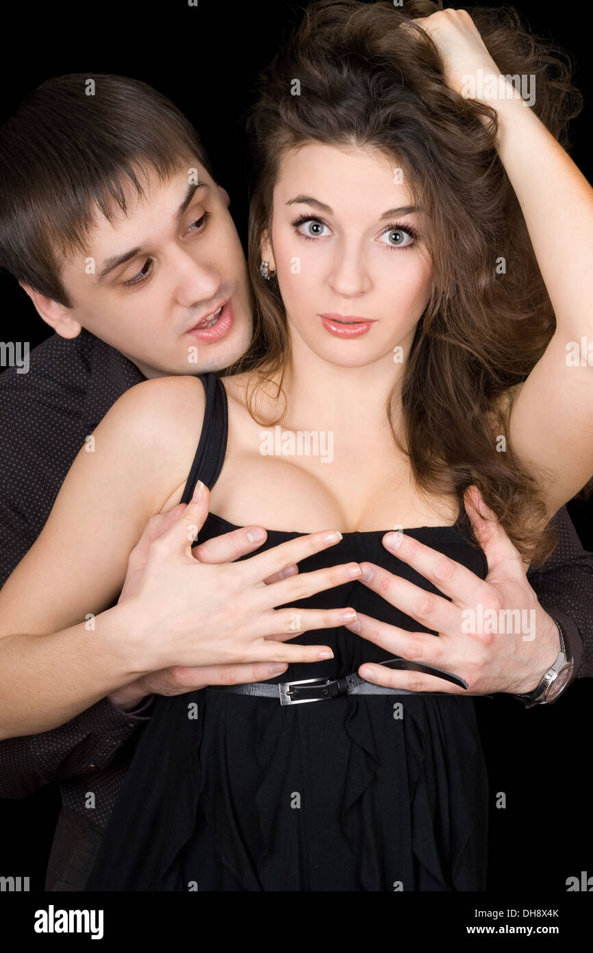 Handsome man holding pretty woman by her breast. Isolated on black