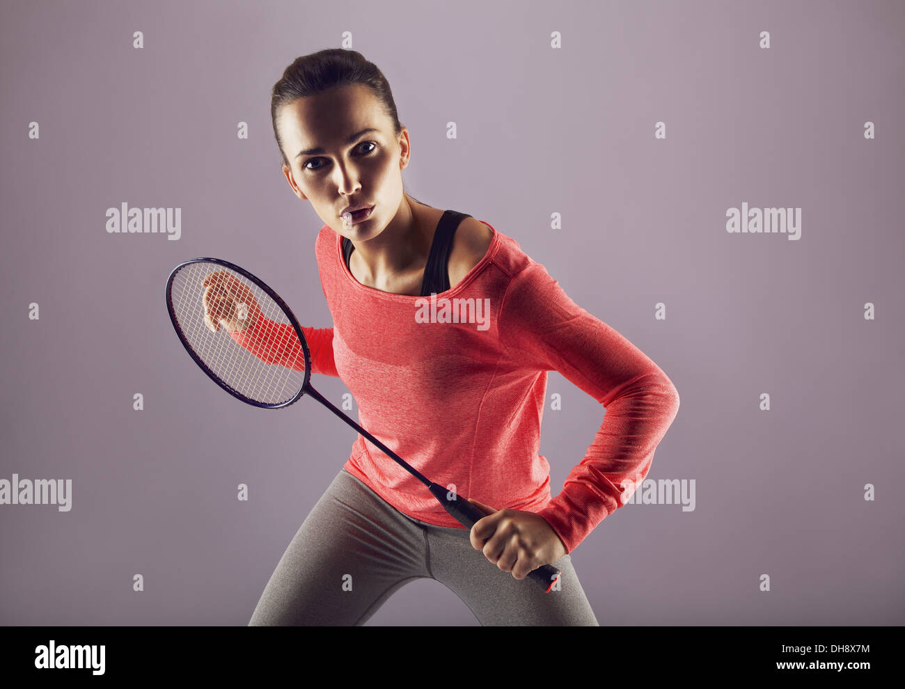 Beautiful girl holding badminton racket playing against grey background. Female sports person badminton player looking at camera Stock Photo