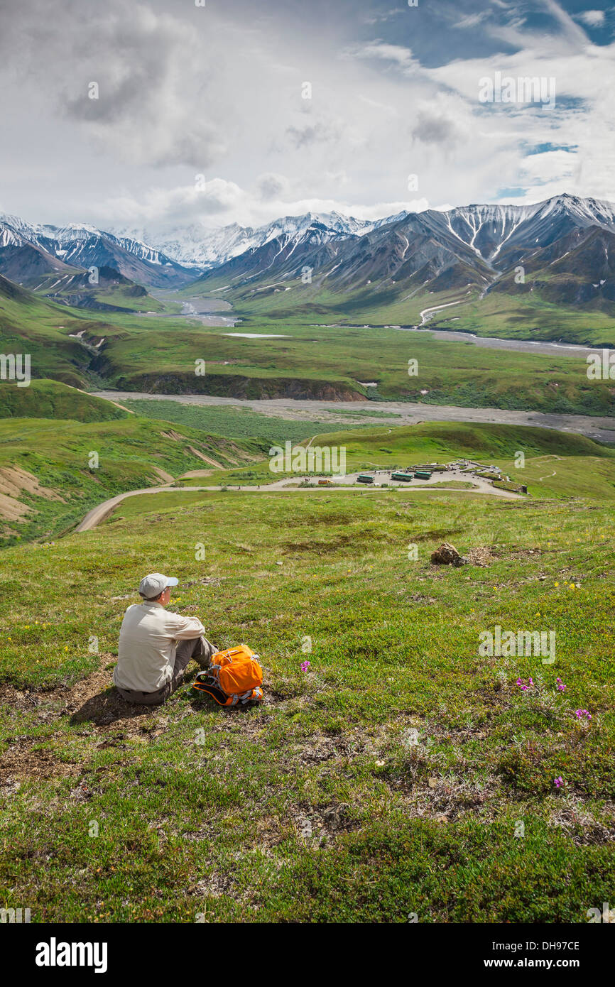 A Male Hiker Sitting On The Tundra On The Mountain Side Looking Down At The Eielson Visitor's Center In Denali National Park Stock Photo