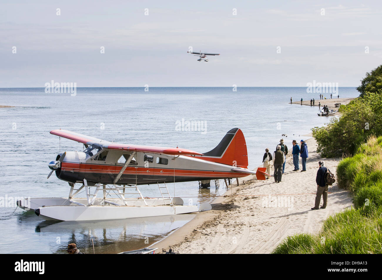 Floatplane Tied To The Sandy Shore Picking Up And Dropping Off Guests With Fishermen And Another Plane In Flight, On The Kvichak River Stock Photo