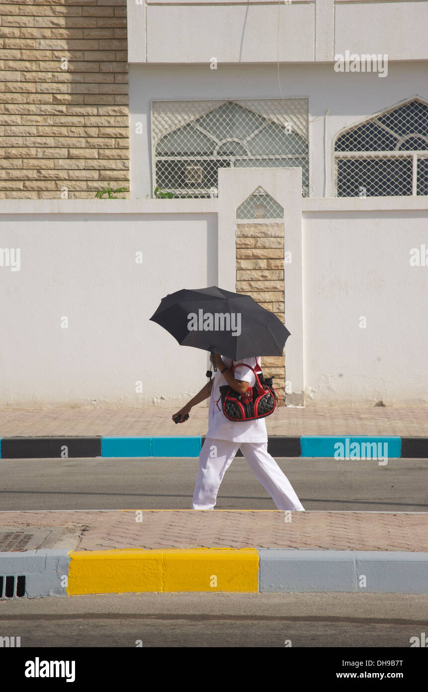 Woman hides from extreme Middle Eastern heat under her umbrella in Abu Dhabi city Stock Photo