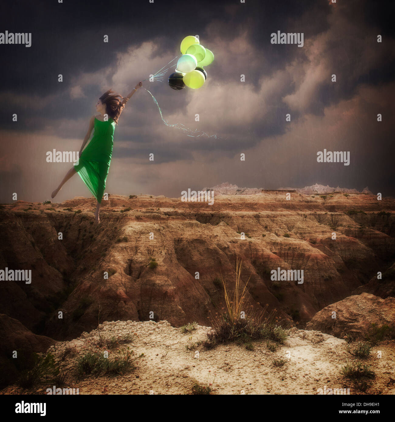 Woman in green dress being pulled bu a bunch of balloons over the badlands of South Dakota. Stock Photo