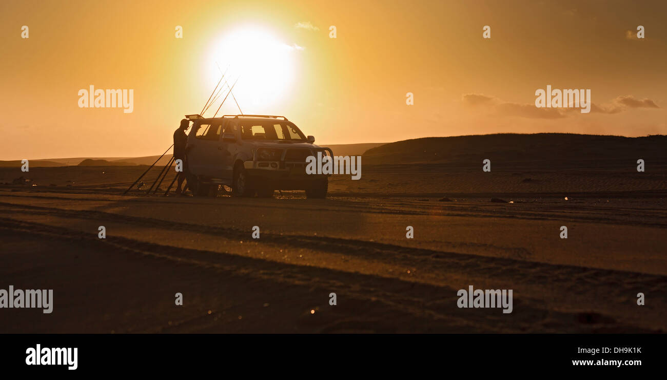 panoramic view of beach sand dune off-road track with parked 4wd vehicle at sunset with fisherman preparing fishing rods against Stock Photo